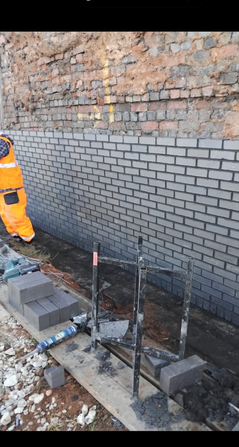 Grey brick wall built against red brick existing