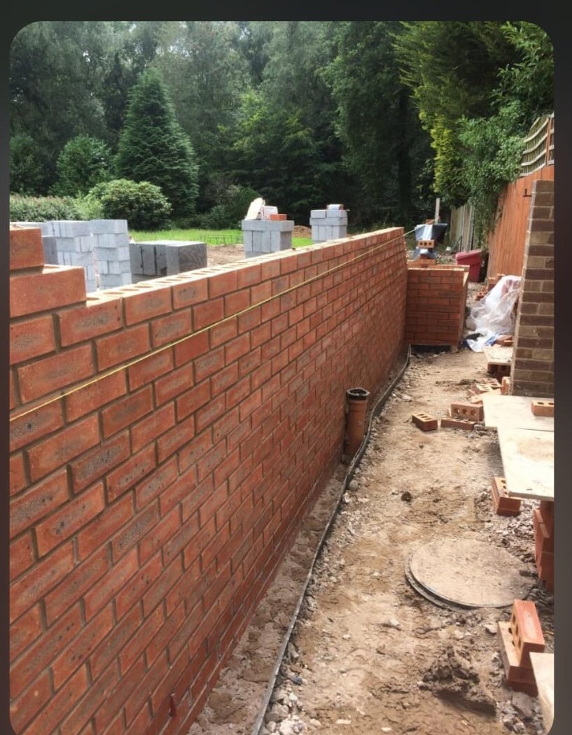 Red brick boundary wall in progress with blocks stacked beside it